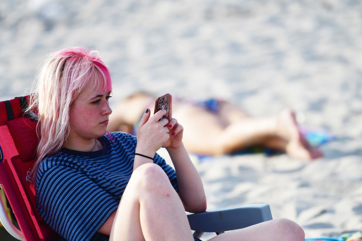 A person sitting on a beach looking at their phone.